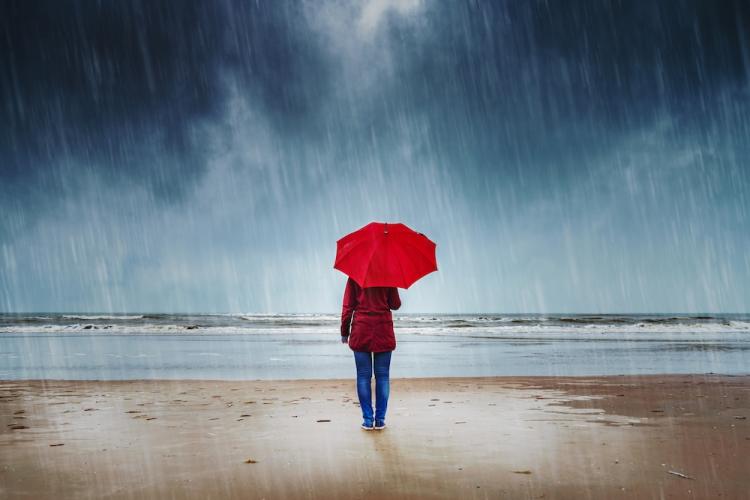 Woman with an umbrella standing in the rain watching the sea.