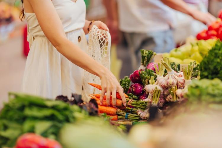 Hands puts fruits and vegetables in cotton produce bag at farmers market.