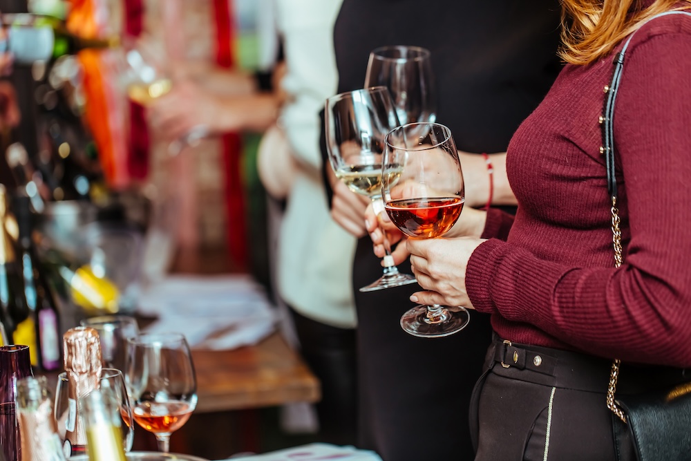 visitors stand near tables with tasting samples and hold glasses of wine.