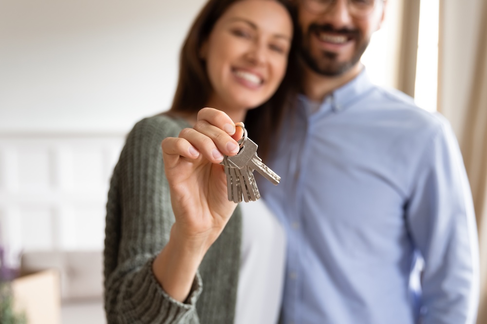 Smiling young couple show house keys moving in together.
