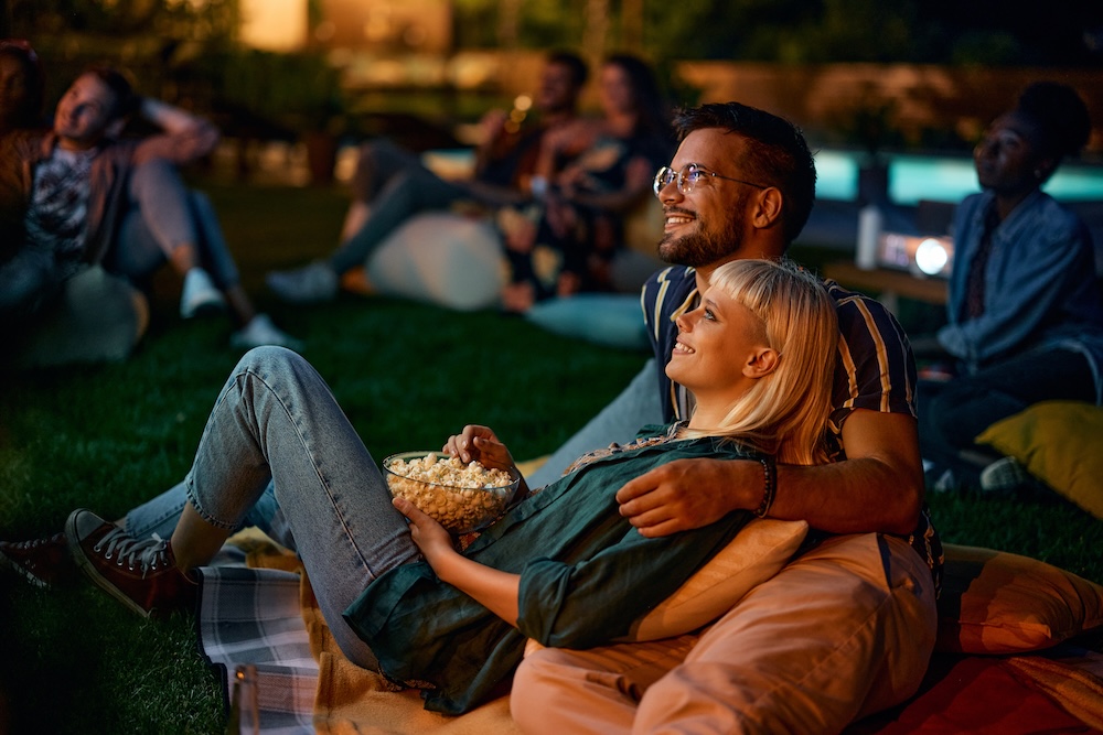 Young couple eating popcorn while watching movie at night.